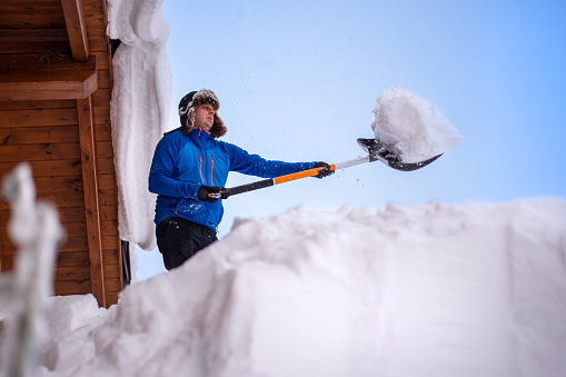 Man cleaning roof of house from snow using snow shovel.