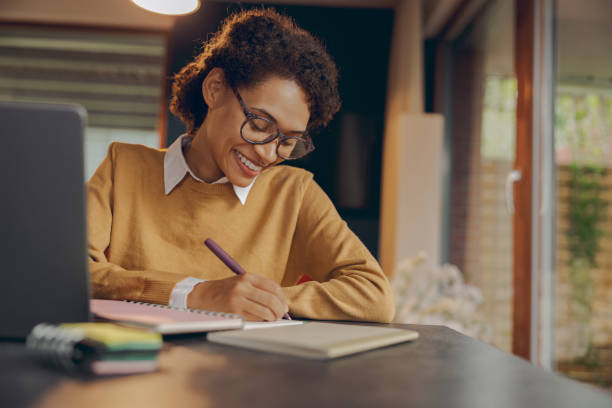 istock Smiling female manager working remotely on laptop from home and making notes 1840352372