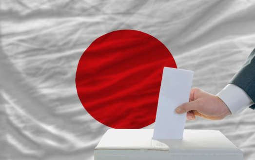 man putting ballot in a box during elections in japan in fornt of flag