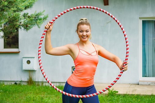 Woman using hoola hoop for slim fit body, doing exercises gym outdoor in garden. Workout training on fresh air. Active healthy lifestyle.