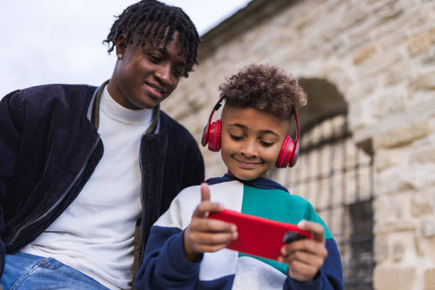 Father and son enjoying a moment together in the park. The son is listening to music with red headphones from his phone. stock photo