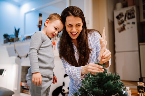 Young mother and her male toddler decorating a Christmas tree