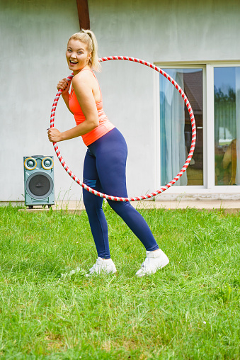 Woman using hoola hoop for slim fit body, doing exercises gym outdoor in garden. Workout training on fresh air. Active healthy lifestyle.