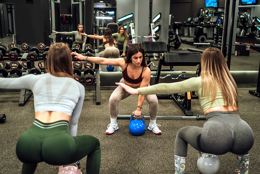 Young woman personal trainer working out with her female clients in the gym