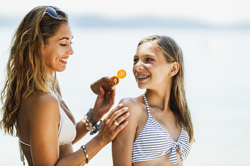 A beautiful teenage girl and her young mother using sun protection cream while enjoying time on the beach.