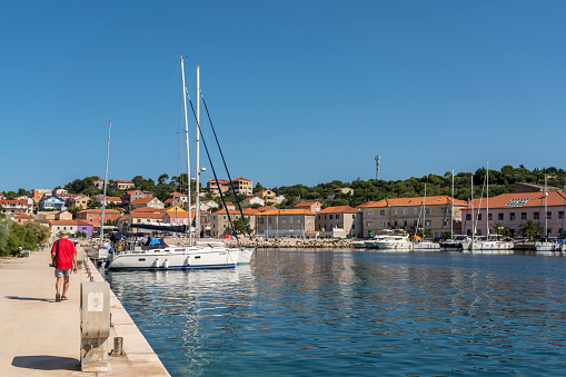 One men walking on pier, at the port with boats in colorful town Sali on Dugi otok, island in Croatia.