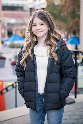 Happy smiling tween girl standing in a puffer jacket outside in an urban area