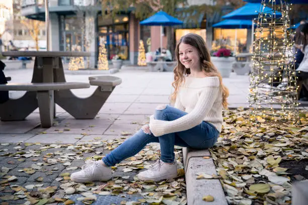 Happy smiling tween girl sitting on a curb outside in an urban area