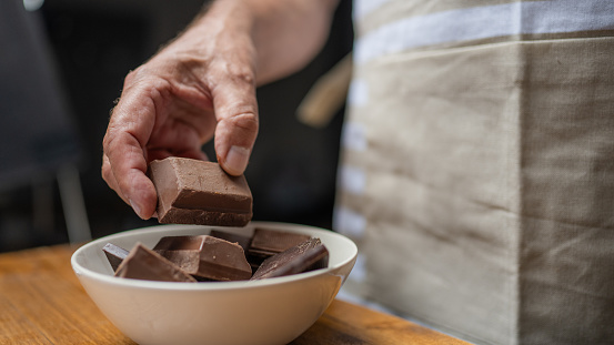 Senior man hands breaking chocolate bar and putting pieces in bowl close up