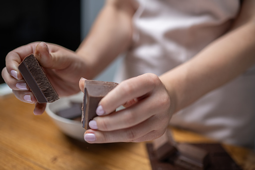 Young woman hands breaking chocolate bar and putting pieces in bowl close up