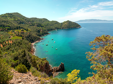 Beautiful mediterranean italian landscape. Aerial view from the panoramic road around the commune of Monte Argentario to the bay of the Cala grande beach. The turquoise waters of the Tyrrhenian Sea are surrounded by lush green hills. Tuscany, Grosseto.