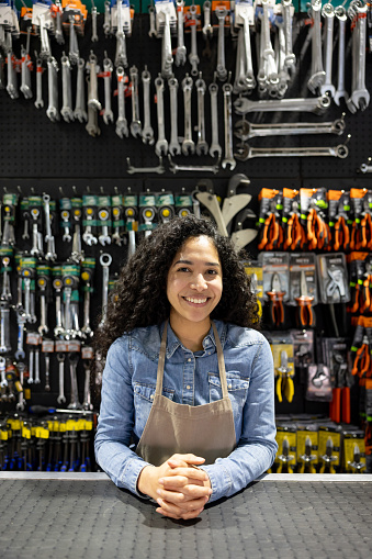 Portrait of a happy saleswoman working behind the counter at a hardware store and looking at the camera smiling