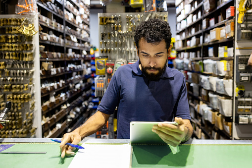 Latin American employee working at a hardware store looking at the inventory on a digital tablet