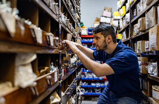 Latin American retail clerk working at a hardware store and searching for screws
