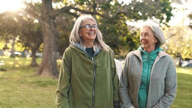Senior friends, walking and talking in park together for morning exercise, bonding and happy conversation. Smile, nature and old people, women trekking in garden with discussion and sunshine in trees