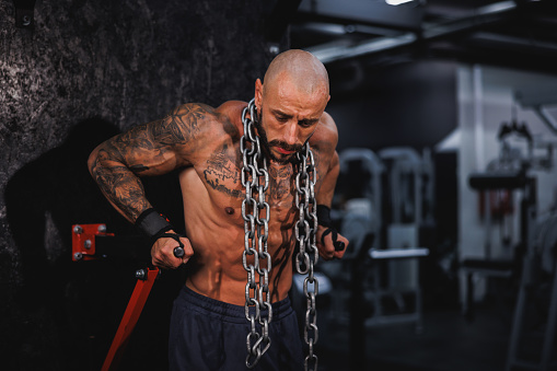 Shot of a young fitness man working out with a heavy chain around his neck in the gym.