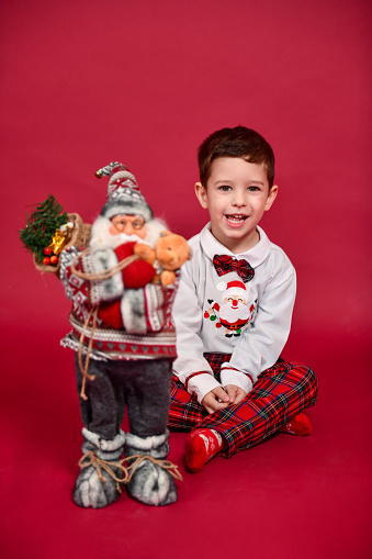 Small Boy In Christmas Outfit Lying Down On Red Carpet And Background