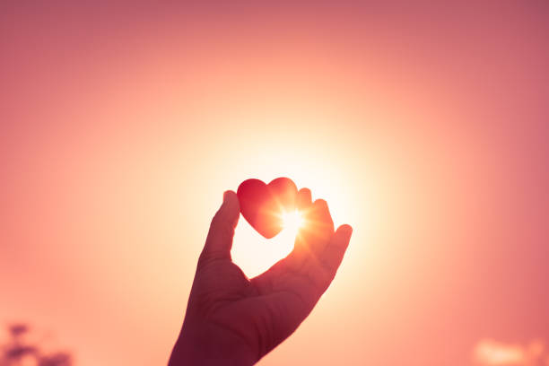 Hand holding heart against a sunset sky.