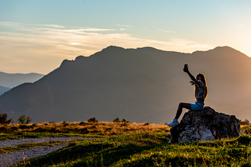 Teenage Girl Sitting on the Rock at the Sunset in Summer, Enjoy the Freedom of the Mountain View Using the Phone