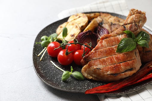 Delicious grilled meat and vegetables on light grey table, closeup