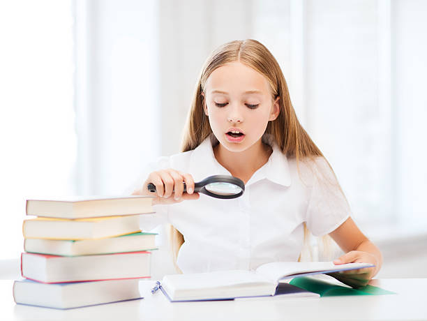 istock girl reading book with magnifier at school 184057727