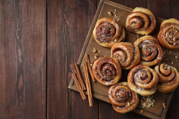 istock Tasty cinnamon rolls, sticks and nuts on wooden table, top view. Space for text 1840593933