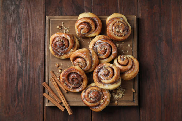 istock Tasty cinnamon rolls, sticks and nuts on wooden table, top view 1840598682