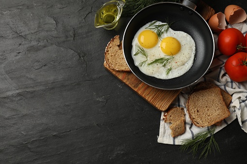 Frying pan with tasty cooked eggs and other products on black table, flat lay. Space for text