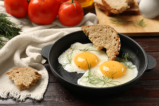 Delicious fried eggs served with bread and tomatoes on wooden table