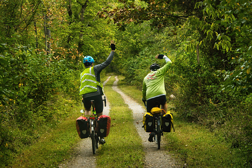 Early Autumn landscape featuring two cyclists, seen from behind, waving goodbye as they ride on the C&O Canal Towpath Trail in Maryland.