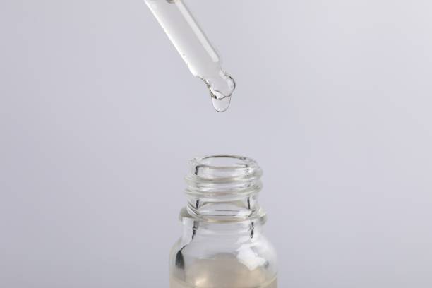 istock Dripping cosmetic serum from pipette into bottle on light grey background 1840664934