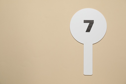 Auction paddle with number 7 on beige background, top view. Space for text