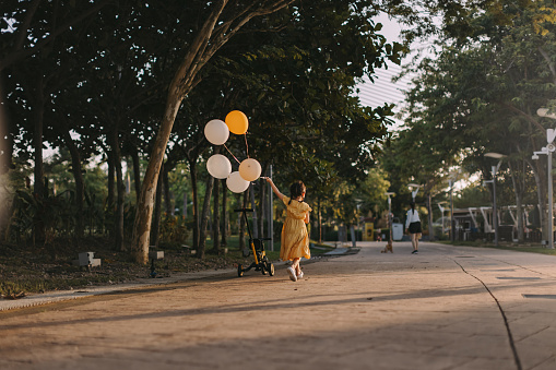 An Asian toddler is running with balloons in a garden park.