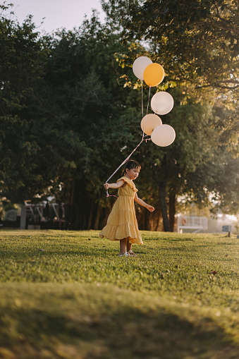 A little girl is turning around with her balloons in a garden park.