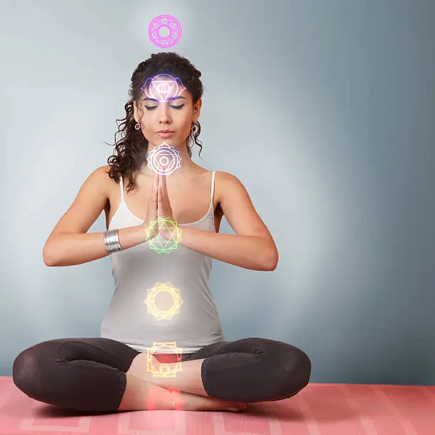 Beautiful young woman doing yoga meditation in lotus position with activated chakras over body