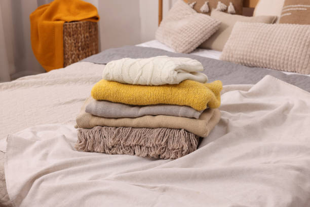 istock Stack of different folded blankets and clothes on bed in room. Home textile 1840694505