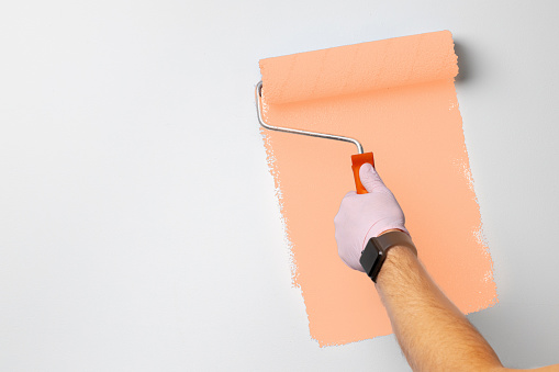 Gloved male hand painting wall into peach color concept