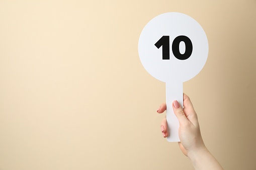 Woman holding auction paddle with number 10 on beige background, closeup. Space for text