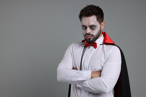 Man in scary vampire costume with fangs on light grey background, space for text. Halloween celebration