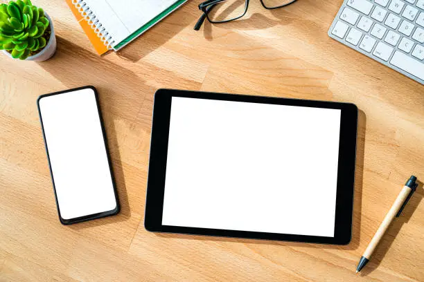 Photo of Overhead view of digital tablet and smartphone with blank screen on wood desk