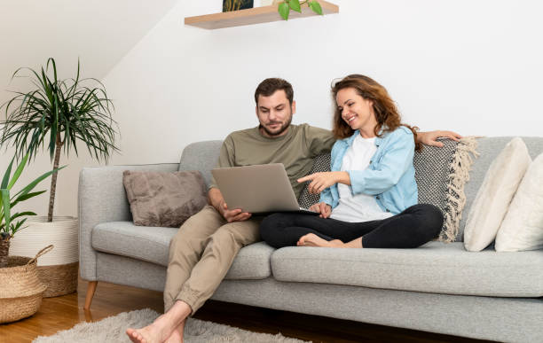 istock Young couple string together on couch at home and using laptop. Online shopping, e-commerce. 1840819977