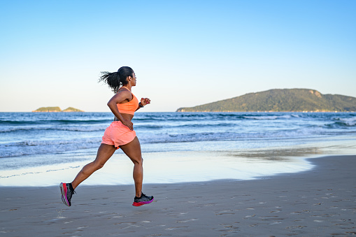 Black woman athlete practicing sports training drill on the beach after sunset in summer