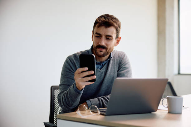 istock Smiling businessman texting on cell phone while working on laptop in the office. 1840862685