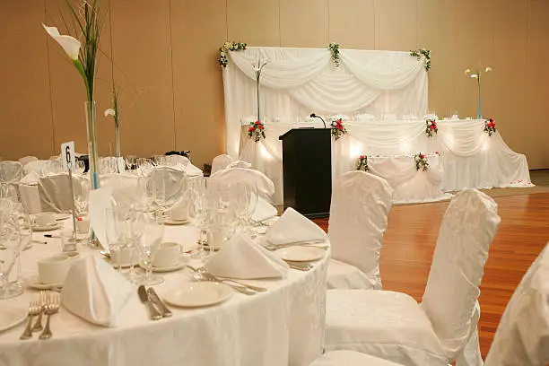 "View of the Head table at the wedding hall dinner party, overlooking guest table in a foreground."