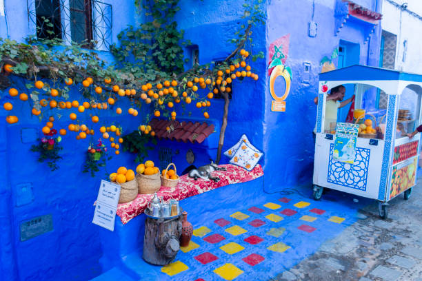 Street juice stand in Chefchaouen medina Chefchaouen, Morocco. October 14th, 2022 - Street juice stand next to a picturesque house with hanging plants with oranges chefchaouen stock pictures, royalty-free photos & images