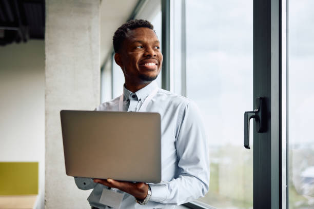 istock Happy black businessman using laptop in the office and looking through the window. 1840873152