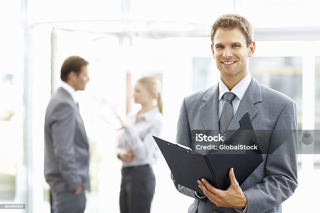 Business man with file Smiling young business man going through document with colleagues discussing in background 20-29 Years Stock Photo