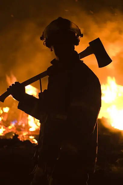 A fireman stands with an axe over his shoulder at a fire. All the firemen in my portfolio would love to see how their images are used. If you have the time to show a sample it is greatly appreciated.