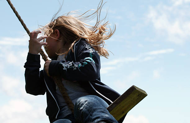 A young girl's hair flows in the breeze as she swings on a rope swing.