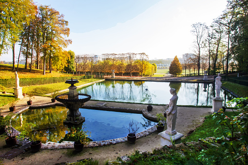 Idyllic landscape with pond, statues, potted plants in Saint-Cloud park. Sunny, orange day in autumn in Paris with autumn leaf color.